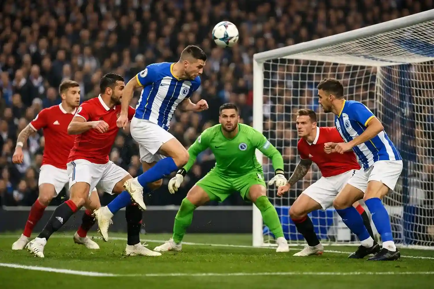 Football players from both teams competing near a goal with goalkeeper preparing to save