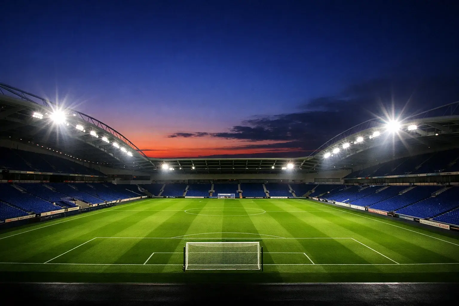 Modern football stadium at dusk with floodlights illuminating the pitch
